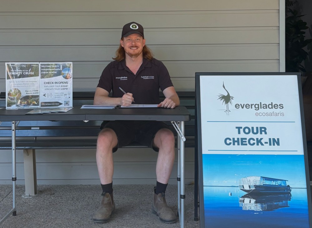 Person at a table for Everglades Tour check-in with signs and brochures.